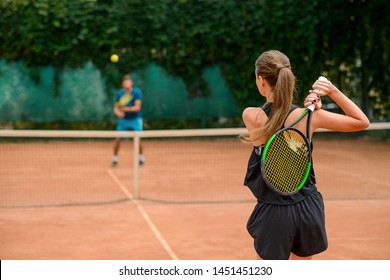 Woman Getting Ready To Shot A Ball, Holding A Racket Behind Back. Couple Playing Tennis In Outdoor Court.