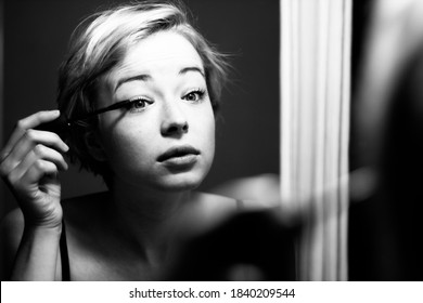 Woman Getting Ready For Work Doing Morning Makeup Routine Applying Mascara In Bathroom Mirror At Home. Beautiful Caucasian Girl Applying Eye Make-up. Black And White Image.