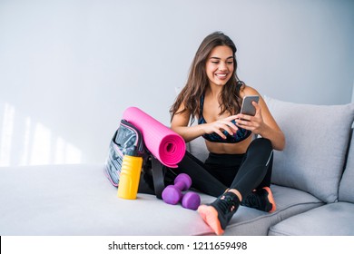 Woman Getting Ready For A Workout. Attractive Sportswoman Getting Ready For Fitness. Ready For The Fitness.  Getting Her Workout Tracks Ready. Female Athlete Using A Mobile Phone In Bed 