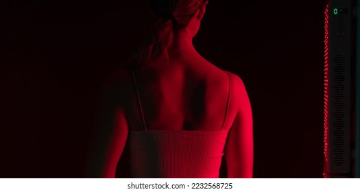 Woman getting red light therapy on her back. Rearview of a woman standing next to a red light device in a beauty salon. Anti-aging cosmetic treatment. - Shutterstock ID 2232568725