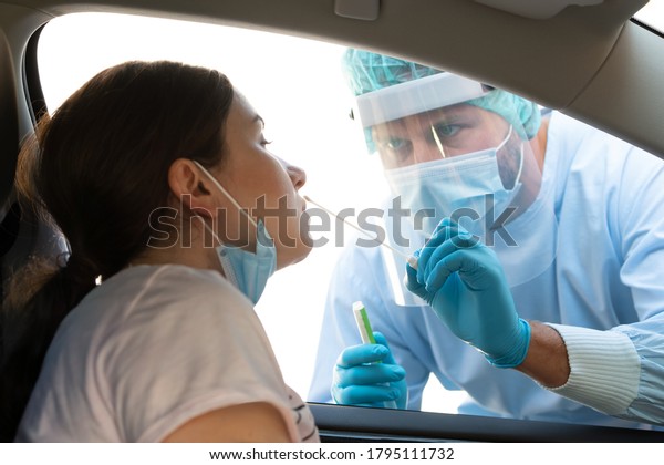 Woman getting tested at a coronavirus\
drive thru station by medical staff with PPE suit by throat swab.\
Health care drive thru service and medical\
concept