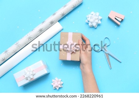 Woman with gift box, bows, scissors, stapler and wrapping paper on blue background