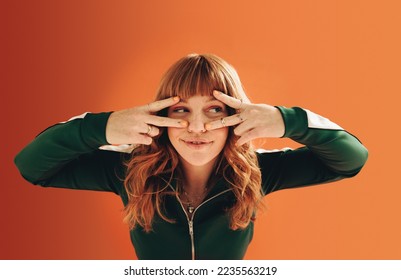 Woman with ginger hair making v signs with her hands. Young woman having fun against an orange background.