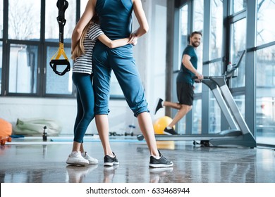 Woman With Girl Looking At Handsome Man Workout On Treadmill At Gym