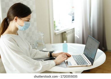 Woman Girl In Medical Mask Works On Laptop Computer, Social Distance During Epidemic Of Influenza Virus Coronavirus Covid-19, Work At Home, Online Training, Health Concept, Hand Sanitizer On The Table