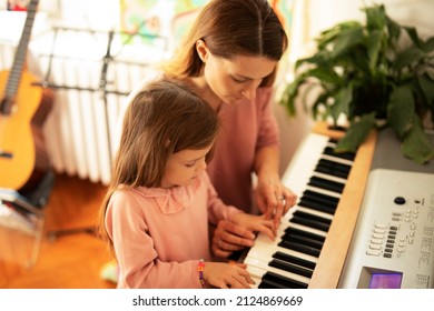 Woman and girl playing a piano. Beautiful mom teaching her daughter playing a piano..	