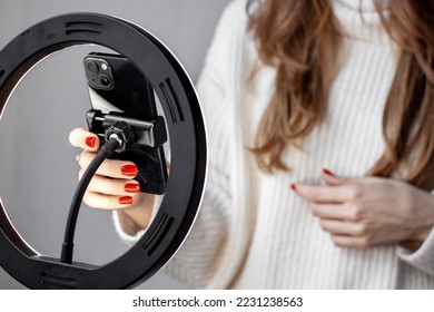 woman girl young blogger vlogger talking with followers hand holding phone in middle of selfie light round lamp.blonde hair red nails female explaining moving hands from side to side or typing 