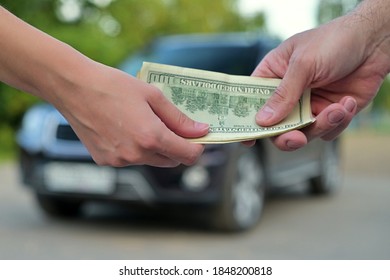 A Woman Gives Cash To A Man When Buying A Car. The Car Is Out Of Focus