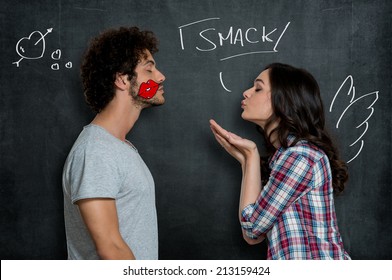 Woman Giving Flying Kiss To Her Boyfriend With Lip Sign On Cheek Over Gray Background