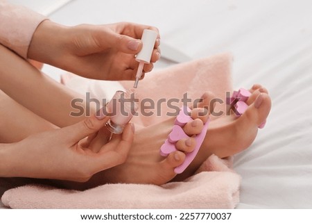 Woman giving herself pedicure on bed at home, closeup