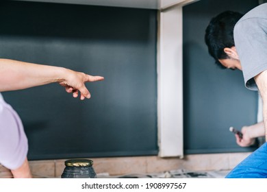 Woman Giving Orders To Her Husband To Indicate Where To Paint On The Wall. Mature Couple Working On Painting The House. DIY Home Decoration Renovation.