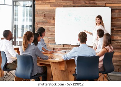 Woman Giving A Presentation At Whiteboard To Business Team