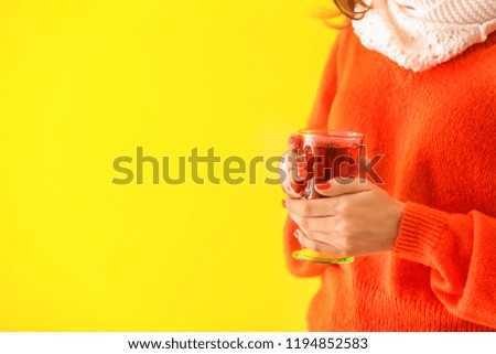 Woman with glass cup of delicious mulled wine on color background, closeup