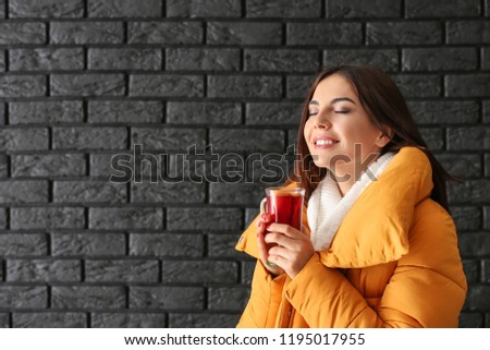 Woman with glass cup of delicious mulled wine against dark brick wall