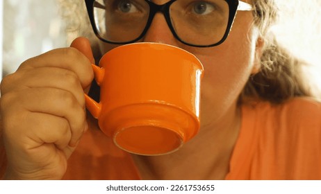Woman with glasses drinking her favourite speciality coffee in a cafe. Girl enjoying hot coffee from an orange mug