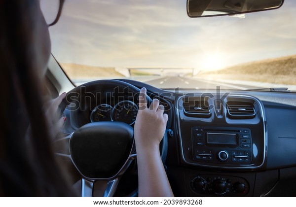 A woman in glasses drives a car at sunset. will\
drive under the bridge. 