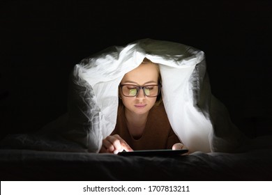 Woman In Glasses Lying In Bed Under The Blanket Using Tablet Late At Night, Can Not Sleep, News Search About Covid-19 Or Sharing Social Media. Insomnia, Nomophobia, Melatonin.  