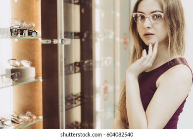 Woman With Glasses In The Optical Salon Standing Next To Showcase Full Of Frames