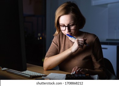 Woman In Glasses Using Calculator To Calculate The Invoice, Planning Expenses, Holding A Pen Near Face, Working On Desktop Pc Late At Night At Home Office, Can Not Sleep. Family Budget, Remote Work. 