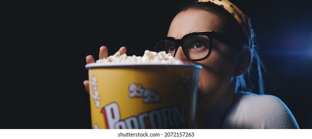 Woman with glasses watching a scary horror movie at the cinema and eating popcorn - Powered by Shutterstock