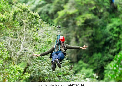 A woman glides on a zipline, hanging from a black wire, in the adventurous town of Banos, Ecuador, surrounded by people and excitement. - Powered by Shutterstock