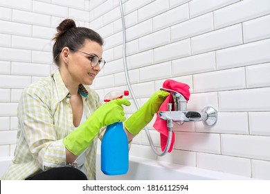 Woman in gloves with detergent and rag doing bathroom cleaning, washing and polishing shower mixer sink, white ceramic tile wall background copy space