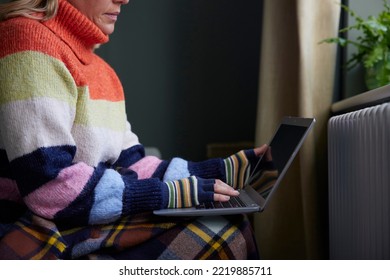 Woman In Gloves With Laptop Trying To Keep Warm By Radiator During Cost Of Living Energy Crisis - Shutterstock ID 2219885711