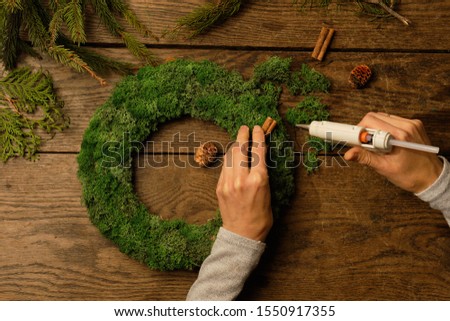 Woman glues decor on a wreath using hot glue. Nearby are natural materials.