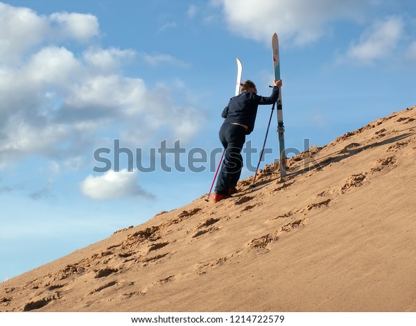 Woman goes uphill of dune\
with skis in her hand. Sand-skiing is sport and form of skiing in\
which skier rides down sand dune on skis, using ski poles. Tver,\
Russia - 2006