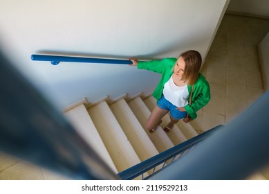 Woman Going Up The Stairs In Apartment House.