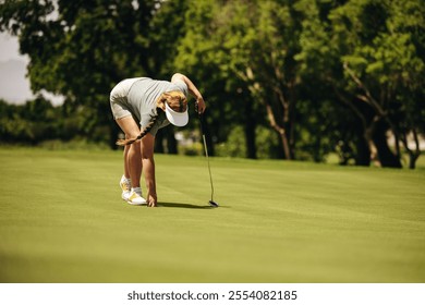 Woman golfer is crouching on the putting green, preparing to take a shot with her golf club on a sunny day. - Powered by Shutterstock