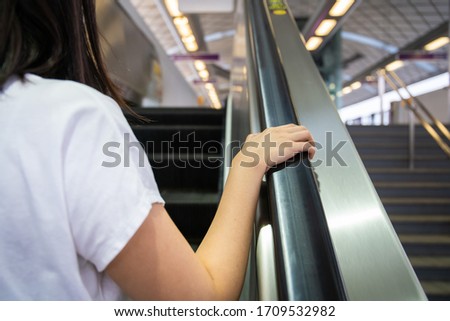 Woman grabbing the escalator hand rail while standing on the escalator, woman going down the stair in the shopping mall by using escalator. Safety awareness in everyday life concept.