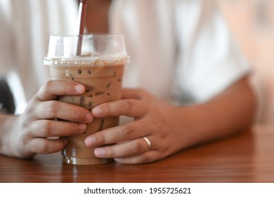 A Woman Grabbing Iced Coffee With Both Hands In The Coffee Shop.