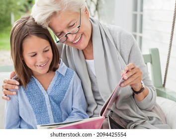 Woman And Granddaughter Reading On Porch Swing