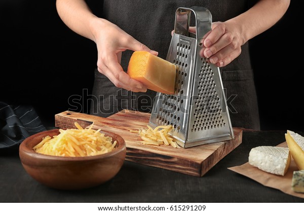 Woman grating cheese on kitchen table.