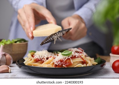 Woman grating parmesan cheese onto delicious pasta at wooden table, closeup - Powered by Shutterstock