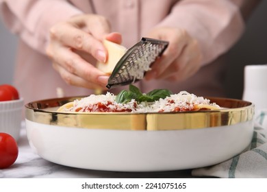 Woman grating parmesan cheese onto delicious pasta at white marble table, closeup - Powered by Shutterstock