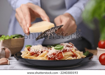 Woman grating parmesan cheese onto delicious pasta at wooden table, closeup