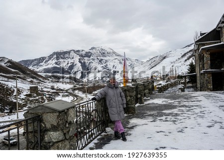a woman in a gray jacket admires the beauty and poses against the background of snow-capped mountains and gorges 