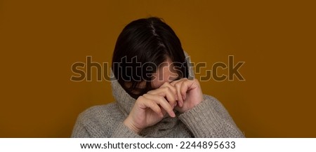 Woman in gray knitted sweater is crying on yellow background. Concept of depression, domestic violence, grief, loss, woe. Girl rubs eyes with her hands from sadness and frustration and wipes her tears