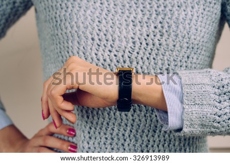 Woman in a gray sweater checks the time on a wrist watch close-up.