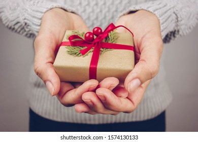 Woman with gray sweater holding a little Christmas present.
