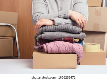 Frau in einem grauen Pullover packt Kleidung in einer Kiste, das Konzept der Hilfe und Freiwilligenarbeit, Bewegung. Verkauf unnötiger Sachen