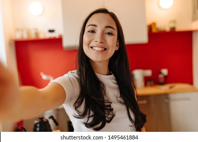 Woman in great mood takes selfie in kitchen. Portrait of brown-eyed girl