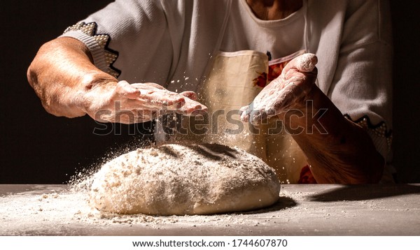 Woman\
great-grandmother clapping hands to dust a mound of freshly\
prepared pastry with flour dough for home\
baking.
