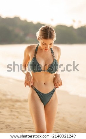Woman in green bikini walking on beach.