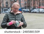 Woman in green coat with pink cast on her arm takes out euro banknotes from an open wallet near a car in a parking lot, High quality photo