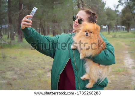 Woman in a green and flowery landscape with her dog in her arms taking a selfie. Idyllic place in spring.