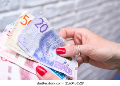 a woman in a green jacket is counting bills of swedish kronor. Swedish currency in various denominations. Concept showing the economic and economic situation in Sweden