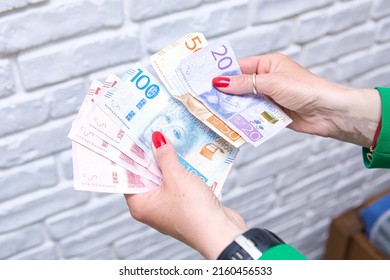 a woman in a green jacket is counting bills of swedish kronor. Swedish currency in various denominations. Concept showing the economic and economic situation in Sweden